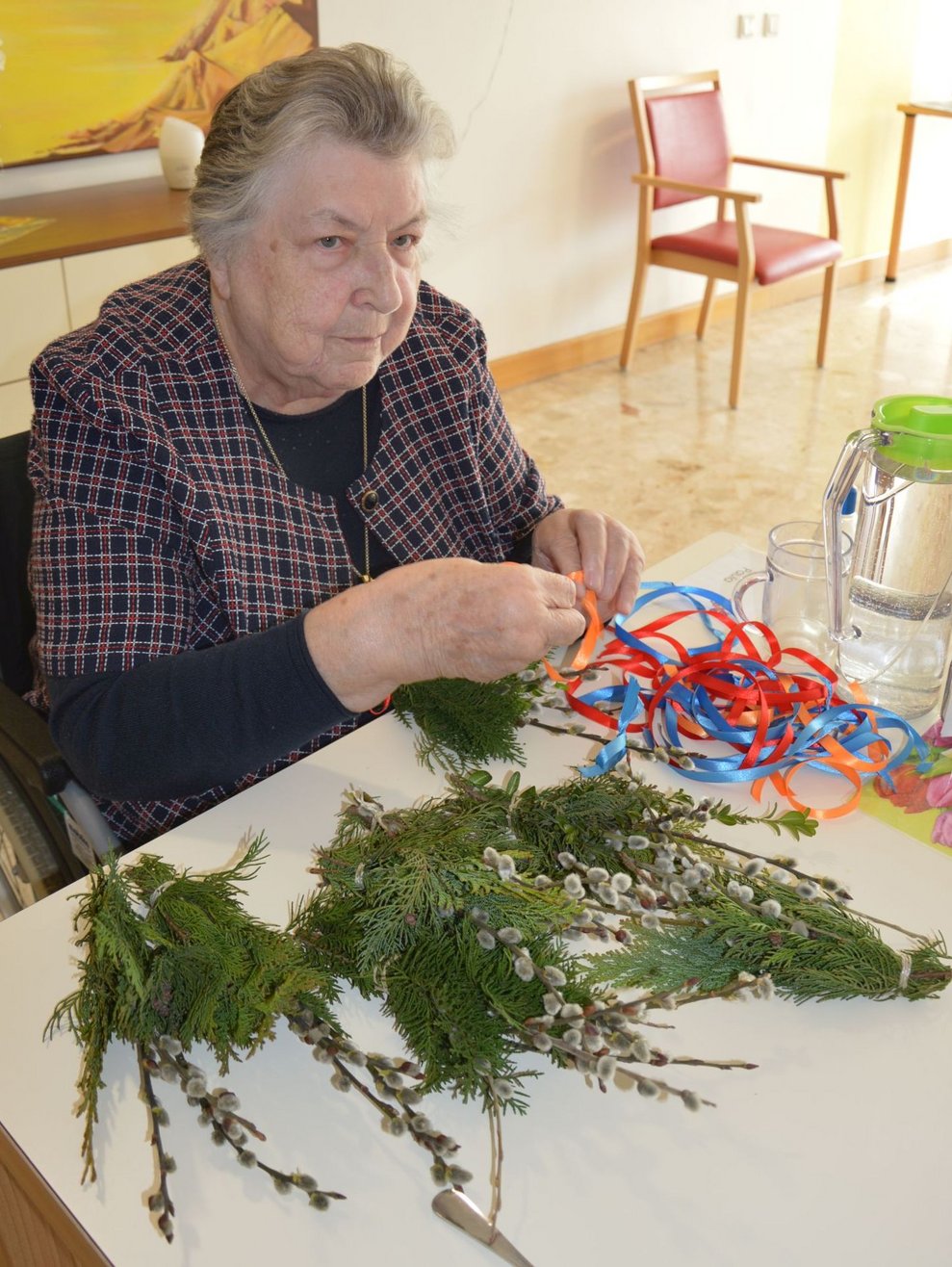 Bewohnerin sitzt vor Palmbesen, die sie gebunden hat.